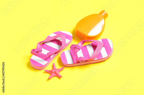 Bottle of sunscreen cream with starfish and flip flops on yellow background