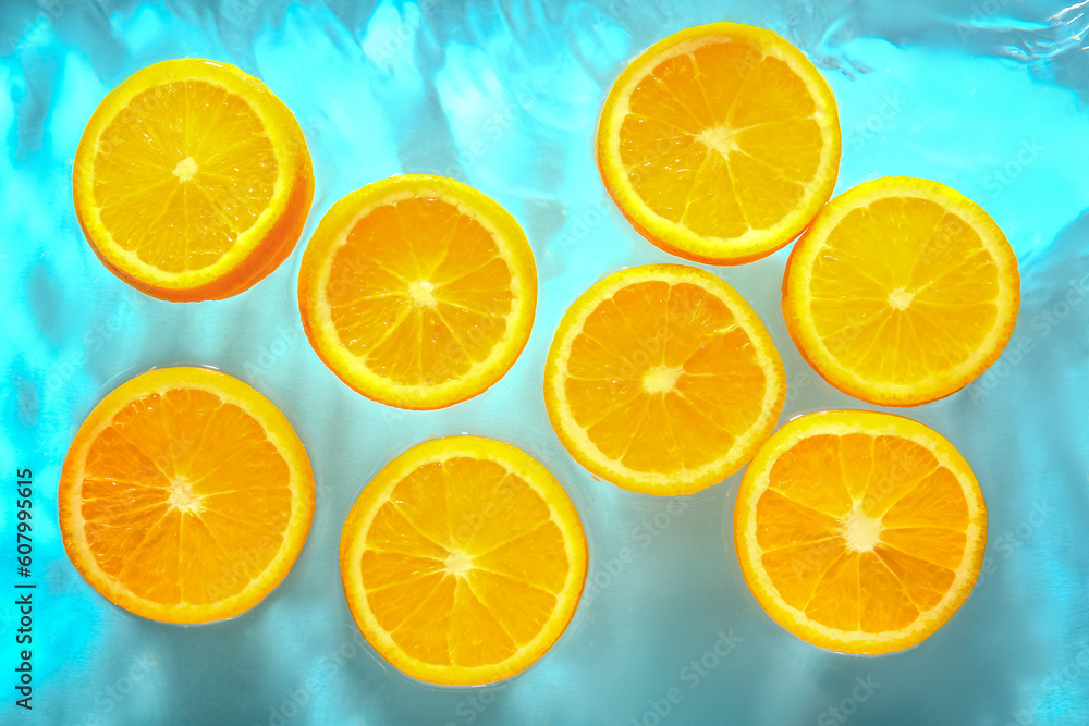 Slices of fresh orange in water on blue background