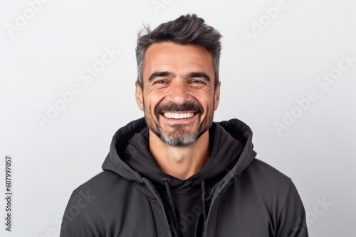 Portrait of handsome young man in black hoodie smiling and looking at camera while standing against white background © Robert MEYNER