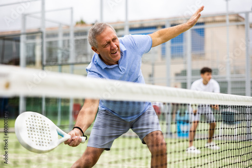 Emotional mature man playing paddle tennis couple match at outdoors court. Health and active lifestyle concept