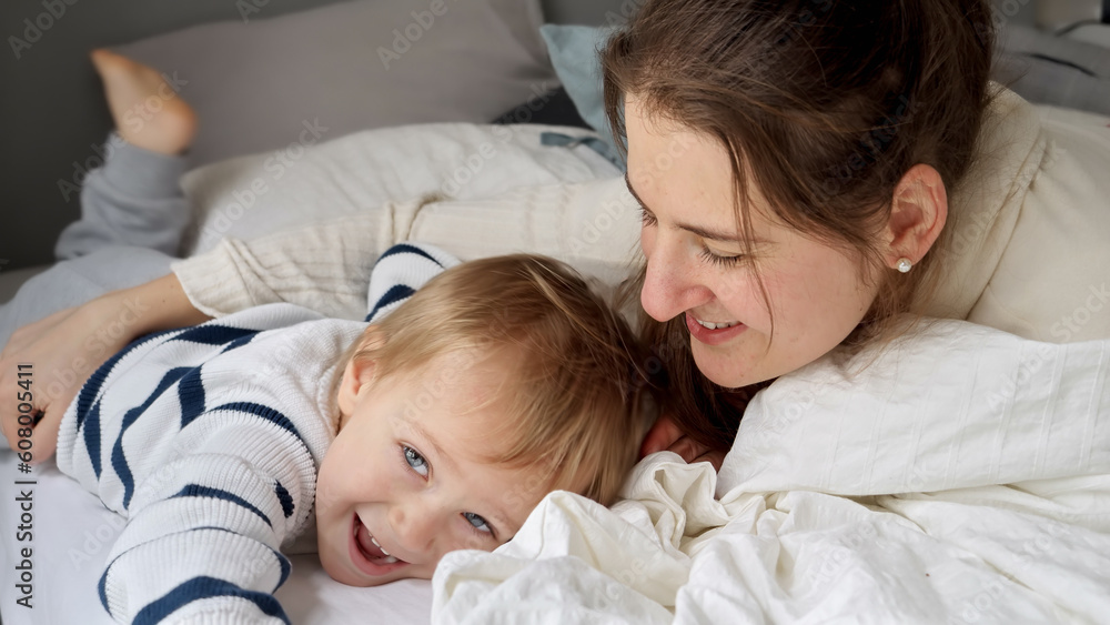 Young loving mother embracing her cute toddler son lying in bed at morning. Concept of family happiness, relaxing at home, having fun in bed, parent and cheerful kids Young loving mother embracing her cute toddler son lying in bed at morning. Concept of family happiness, relaxing at home, having fun in bed, parent and cheerful kids