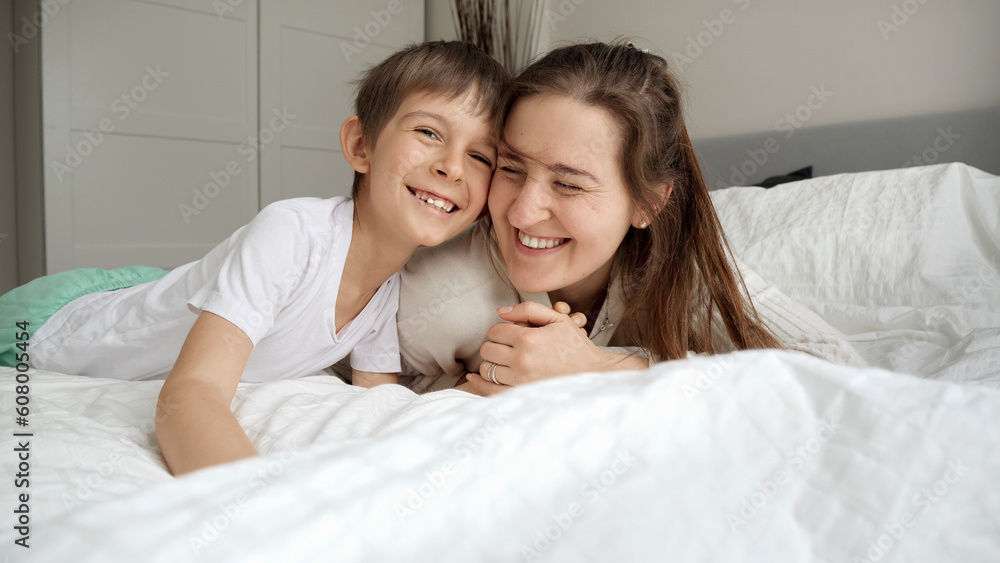 Happy cheerful boy with mother wearing pajamas lying in bed and having good time together Happy cheerful boy with mother wearing pajamas lying in bed and having good time together