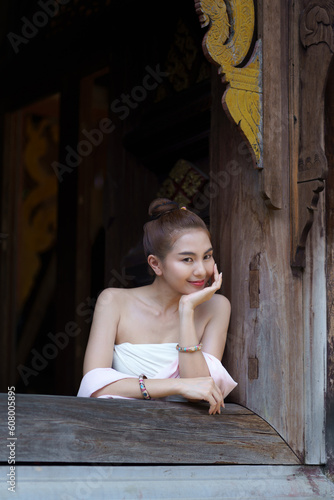 A pretty Asian girl wearing a traditional Thai dress in the countryside sits happily by the window of a beautiful ancient house in Chiang Mai the Northern of Thailand.