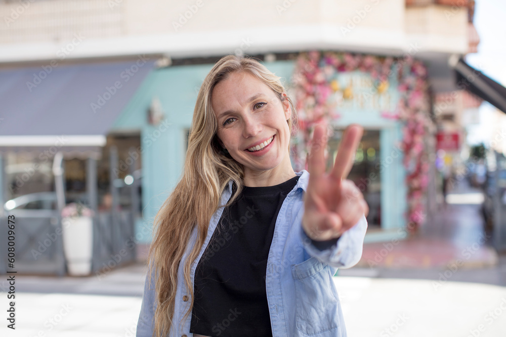pretty woman smiling and looking happy, carefree and positive, gesturing victory or peace with one hand