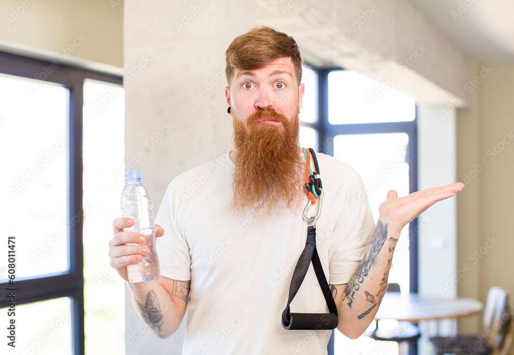 red hair man shrugging, feeling confused and uncertain with a water bottle. fitness concept red hair man shrugging, feeling confused and uncertain with a water bottle. fitness concept