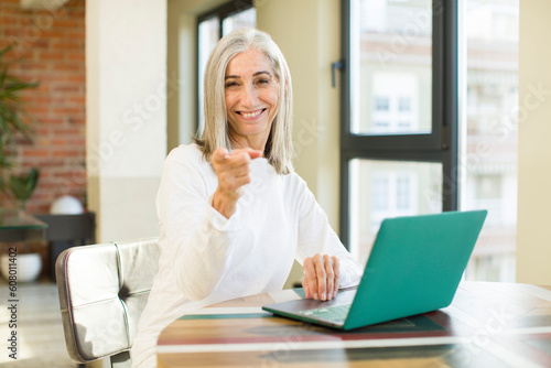 senior pretty woman smiling cheerfully, feeling happy and pointing to the side with a laptop