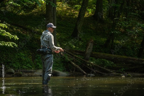 Fisherman catching brown trout on spinning tackle standing in river.