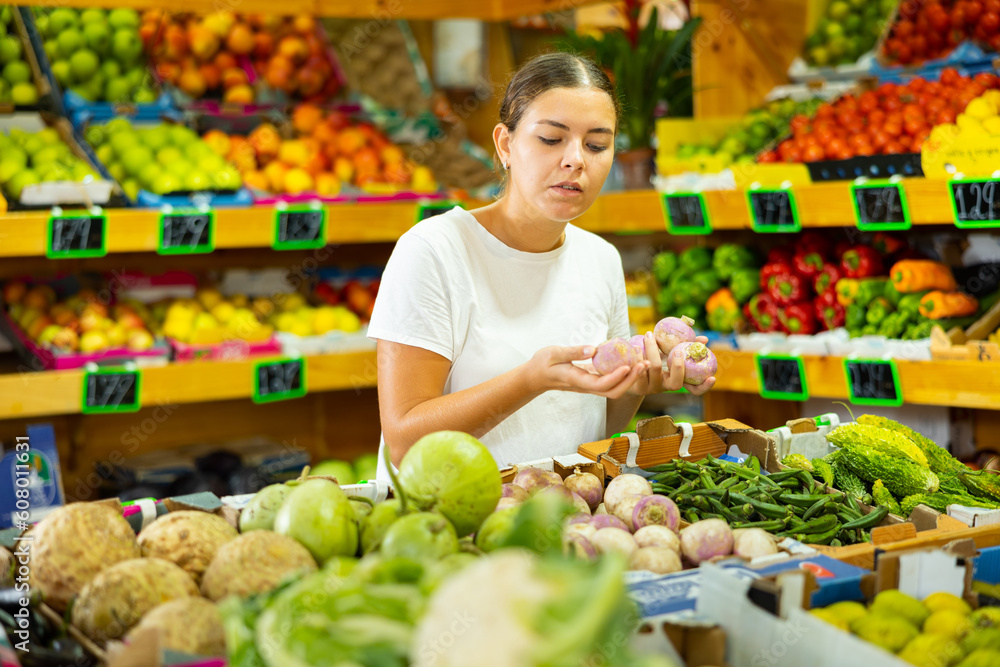 Focused young woman shopper chooses ripe watermelon radish at grocery supermarket