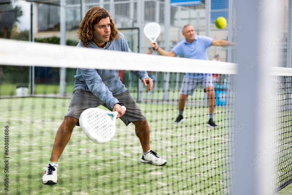 Athletic man plays padel. View through the tennis net