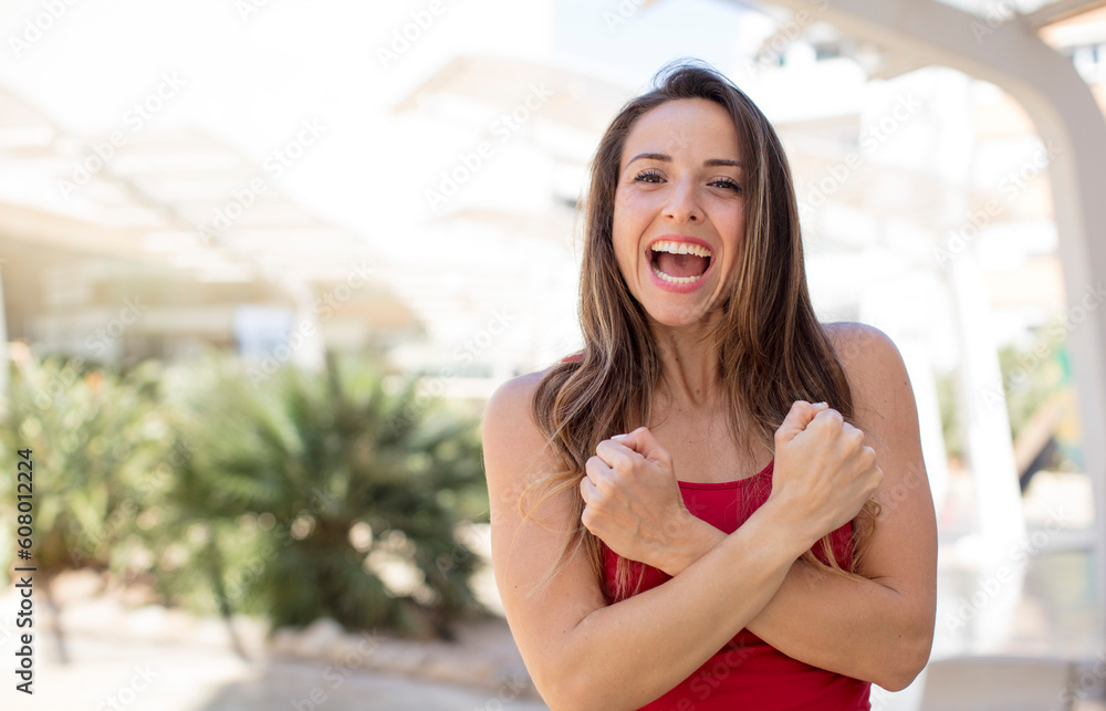 pretty woman smiling cheerfully and celebrating, with fists clenched and arms crossed, feeling happy and positive