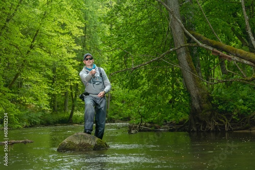 Fisherman catching brown trout on spinning tackle standing in river.