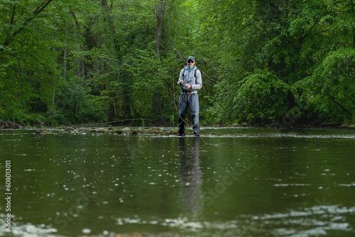 Fisherman catching brown trout on the fly standing in river.