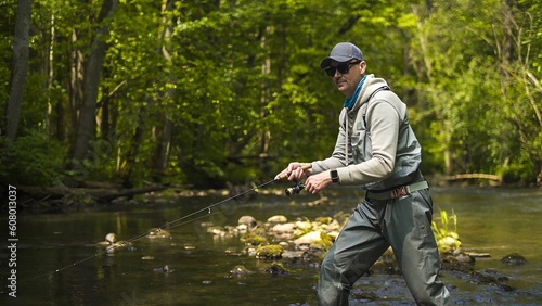 Fisherman catching brown trout on spinning tackle standing in river.