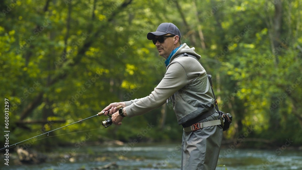 Fototapeta premium Fisherman catching brown trout on spinning tackle standing in river.