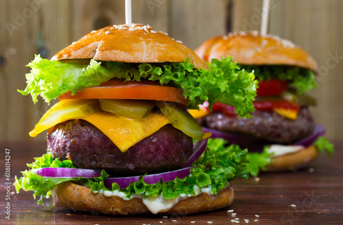 Two juicy hamburgers with cheese, fresh tomatoes, onion and lettuce leaves on wooden surface