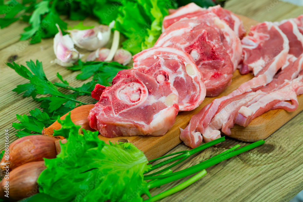 Raw lamb meat on wooden cutting board on background with fresh vegetables and greens