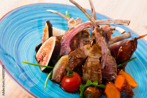 Roasted ribs of mutton served with ripe figs, baked carrots, fresh tomatoes and herbs with sauce demi-glace photo