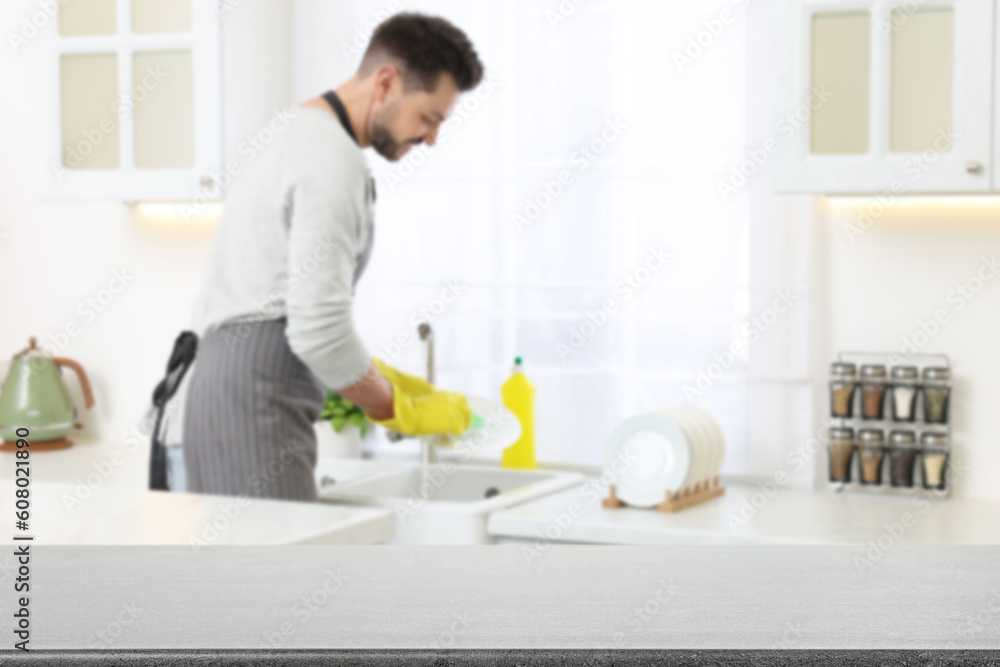 Man doing washing up in kitchen, focus on empty grey stone table Man doing washing up in kitchen, focus on empty grey stone table