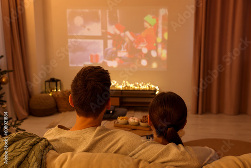 Couple watching Christmas movie via video projector in cosy room, back view. Winter holidays atmosphere