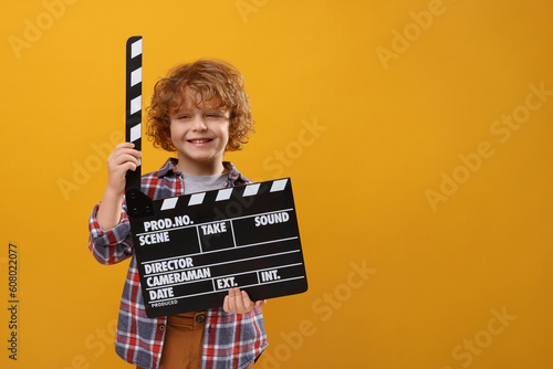 Smiling cute boy with clapperboard on orange background, space for text. Little actor