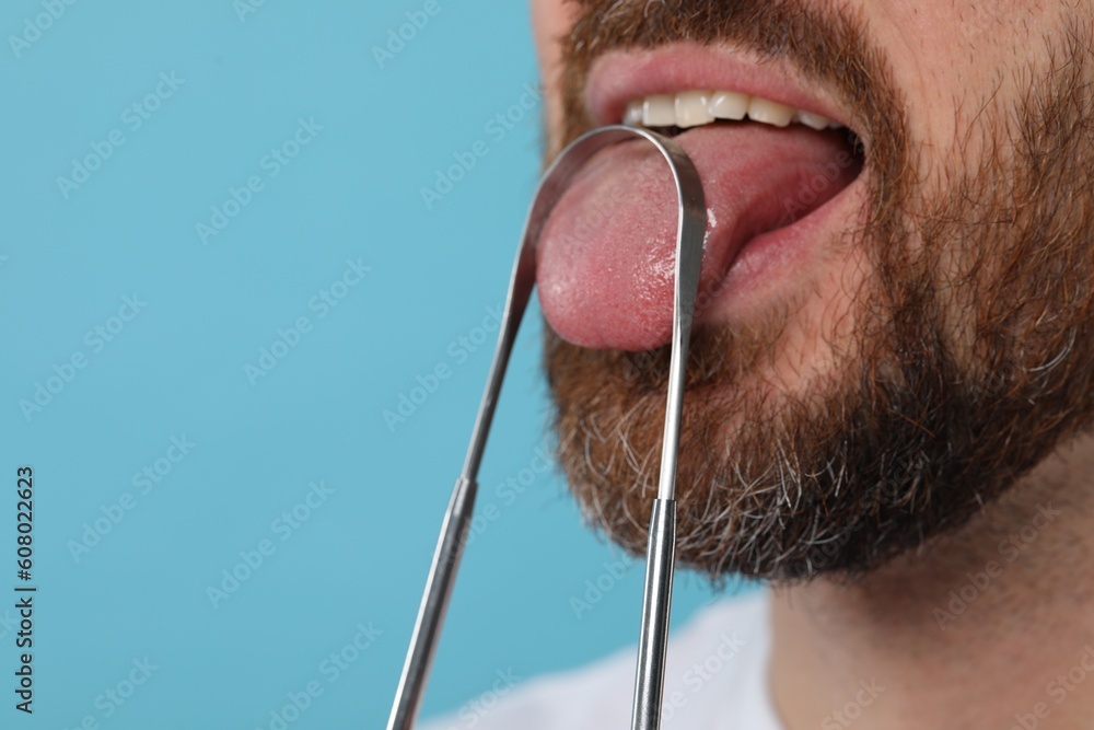 Man brushing his tongue with cleaner on light blue background, closeup. Space for text - obrazy, fototapety, plakaty 