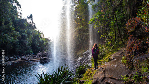 A beautiful girl enjoys a walk behind a spectacular tall waterfall while hiking the Warrie Circuit trail in Springbrook National Park  Gold Coast  Queensland  Australia