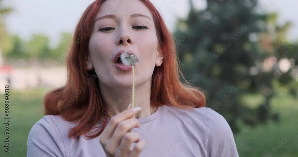 The joyous moments of a young woman blowing on a dandelion she found in the park and directing it towards the camera capture a sense of whimsy and hope The joyous moments of a young woman blowing on a dandelion she found in the park and directing it towards the camera capture a sense of whimsy and hope