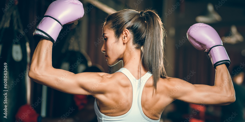 Fototapeta premium sporty athlete young Asian woman wearing sportswear and pink punching gloves practicing boxing martial arts. fit attractive female doing boxing at the fitness kickboxing gym, Portrait of female boxer