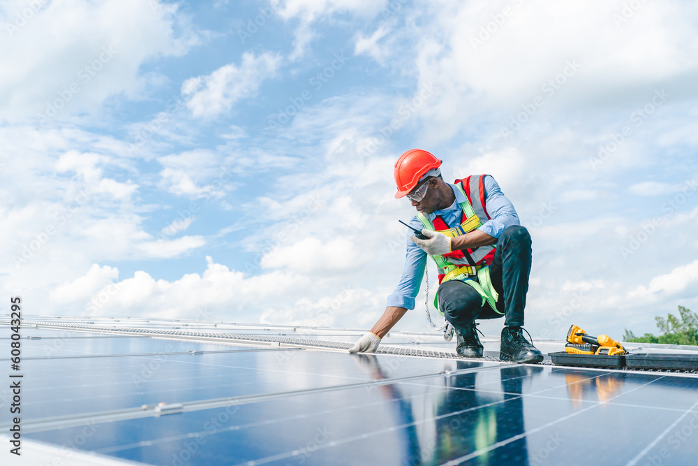 African American engineer maintaining solar cell panels on factory building rooftop. Technician working outdoor on ecological solar farm construction. Renewable clean energy technology concept African American engineer maintaining solar cell panels on factory building rooftop. Technician working outdoor on ecological solar farm construction. Renewable clean energy technology concept