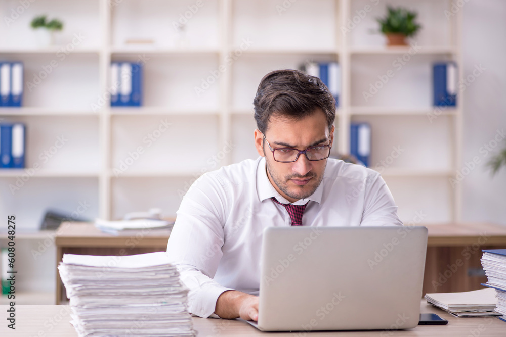 Young male employee and too much work at workplace Young male employee and too much work at workplace