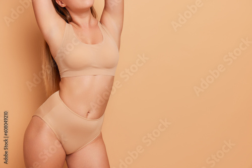 Close-up photo of body positive girl torso in beige sport bra and panties stands on pink background with her hands behind her head, body comfort concept, copy space