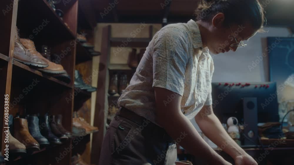Asian man lacing old leather boots, working in a restoration workshop or vintage consignment store, preparing items for sale Asian man lacing old leather boots, working in a restoration workshop or vintage consignment store, preparing items for sale