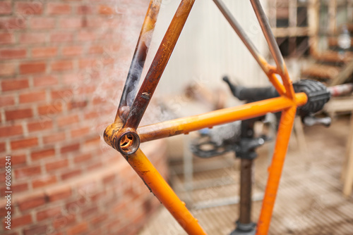 Manual bicycle renovation work, paint removal process using a torch fire to change the color of a bike frame. Selective focus on the tube area with fire and smoke.