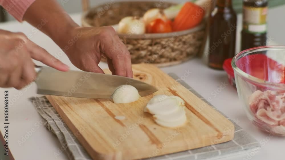 Woman hand using knife to cut white onion on wooden cutting board. Woman preparing food in the kitchen at home. Woman hand using knife to cut white onion on wooden cutting board. Woman preparing food in the kitchen at home.