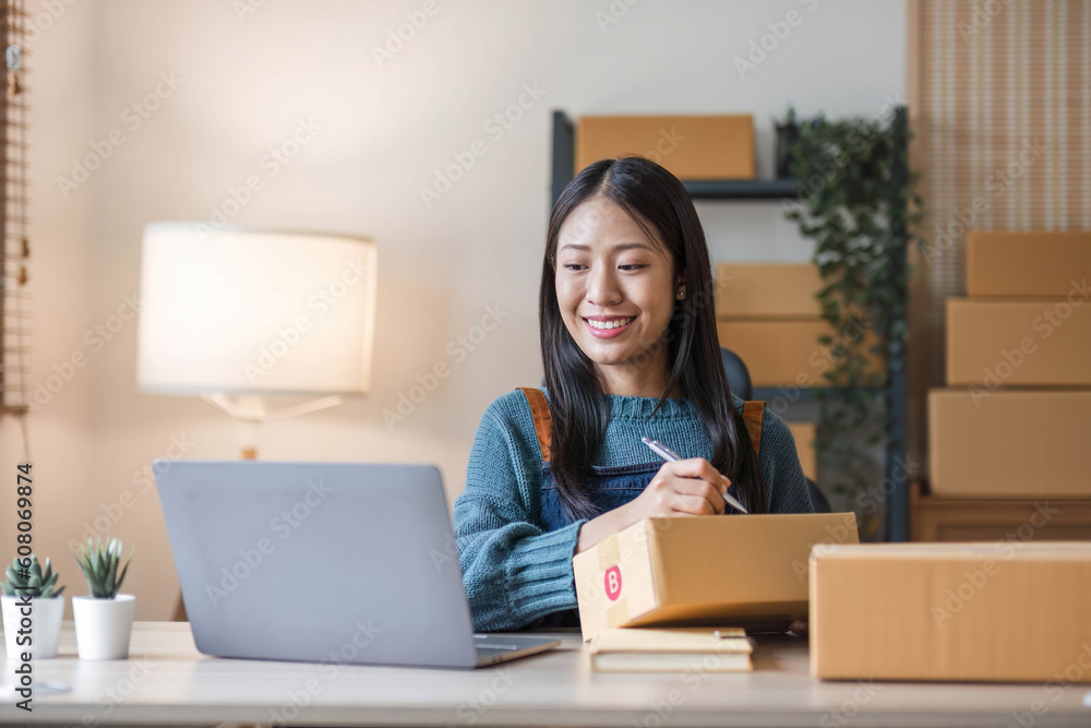 Young beautiful happy asian business woman owner of SME online using laptop receive order from customer with parcel box packaging at her startup home office, online business seller Young beautiful happy asian business woman owner of SME online using laptop receive order from customer with parcel box packaging at her startup home office, online business seller