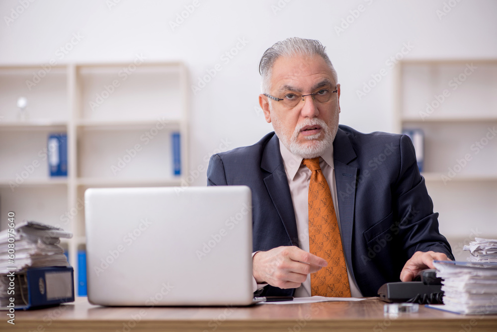 Old male employee speaking by phone at workplace Old male employee speaking by phone at workplace