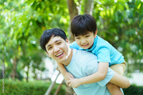 Happy Asian family concept, little happy young boy playing with his father at the garden, a boy climbing on his father back. Asian dad and son portrait.
