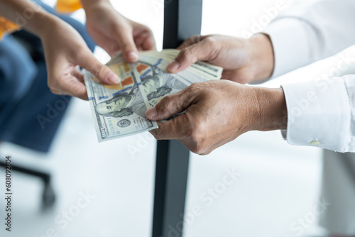Businesswoman hand holding bribe money to government officials sign contracts for business projects, put money under envelope, ideas of corruption and anti-bribery.
