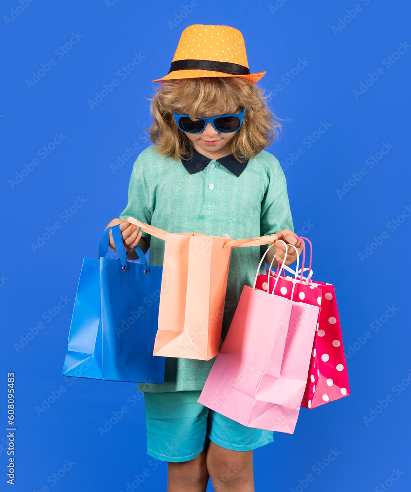Kid boy in fashion clothes goes shopping. Kid with shopping packages. Shopper child with carrying shopping bags.