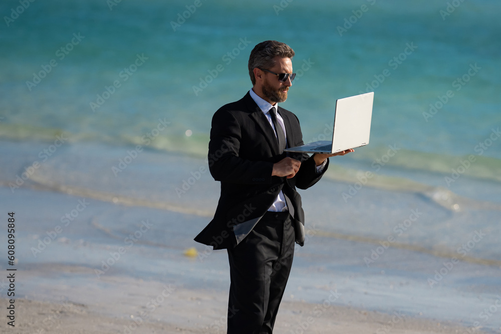 Summer business travel. Business success. Freelance, business work outdoor, online business, e-working. Summer businessman in suit remote working on laptop in sea water. Funny summer businessman.