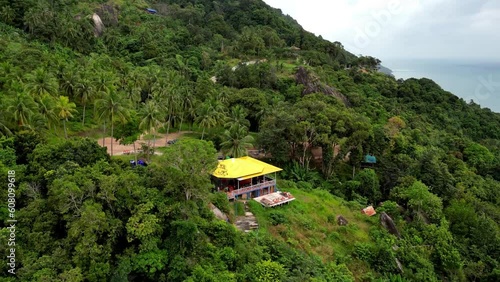 Drone shot of Tomorrowland cafe, wow viewpoint party location. Techno festival on Koh Phangan in Thailand. House on hilltop surrounded by palm trees and jungle. pick up Trucks in front of the house. photo