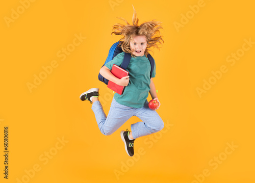Back to school. Full length body of cheerful school child jumping running back to school isolated over yellow background.