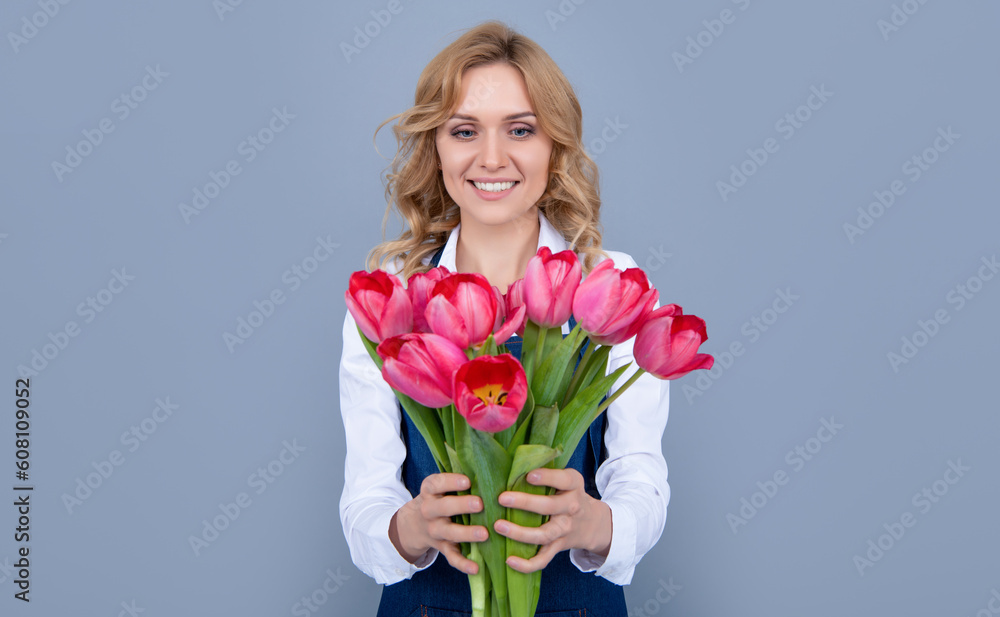 cheerful young woman in apron with spring tulip flowers on grey background cheerful young woman in apron with spring tulip flowers on grey background