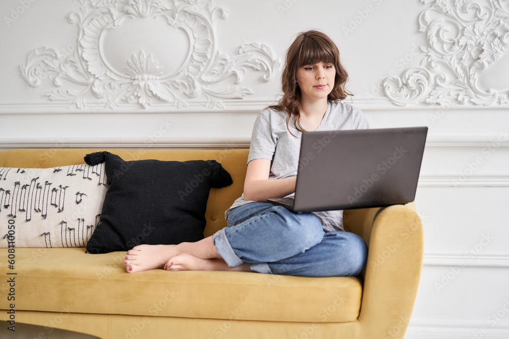 Young casual woman using black laptop while sitting on sofa in living room at home. Beautiful cheerful girl using laptop for communication and work. Stay home Young casual woman using black laptop while sitting on sofa in living room at home. Beautiful cheerful girl using laptop for communication and work. Stay home
