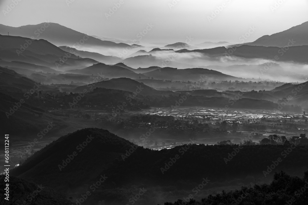 Black and white landscape photo of hills, valleys, forests, fields and villages with clouds over the mountains in the morning.