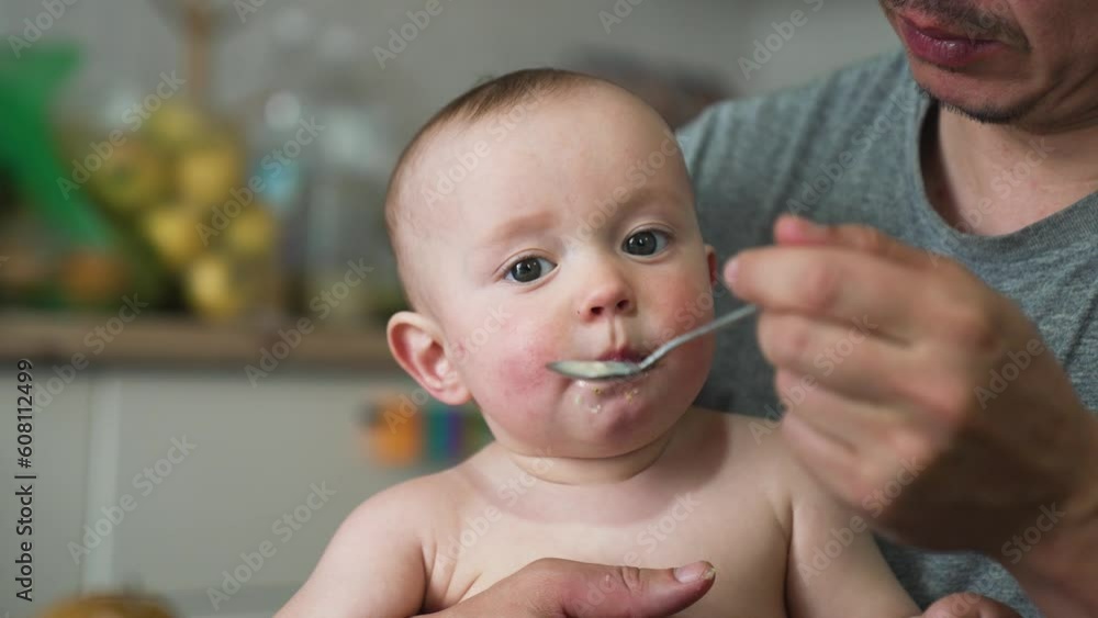 Baby feeding.Parent feed baby porridge.Child sits at table on chair