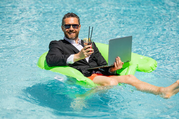 Crazy summer. Business drink summer cocktail and using laptop in suit in water pool. Fun business lifestyle. Funny middle aged business man dreams about summer. Summer travel. Business success.
