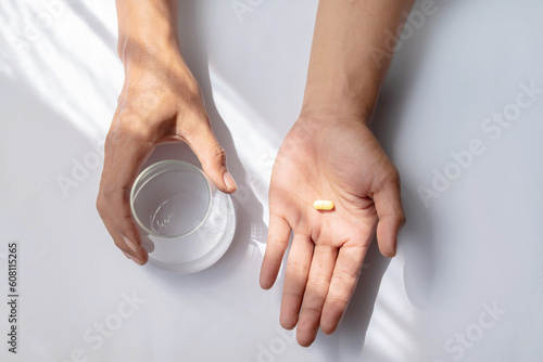 Asian man holding pills and glass of water isolated on white background. Health care and medicine concept
