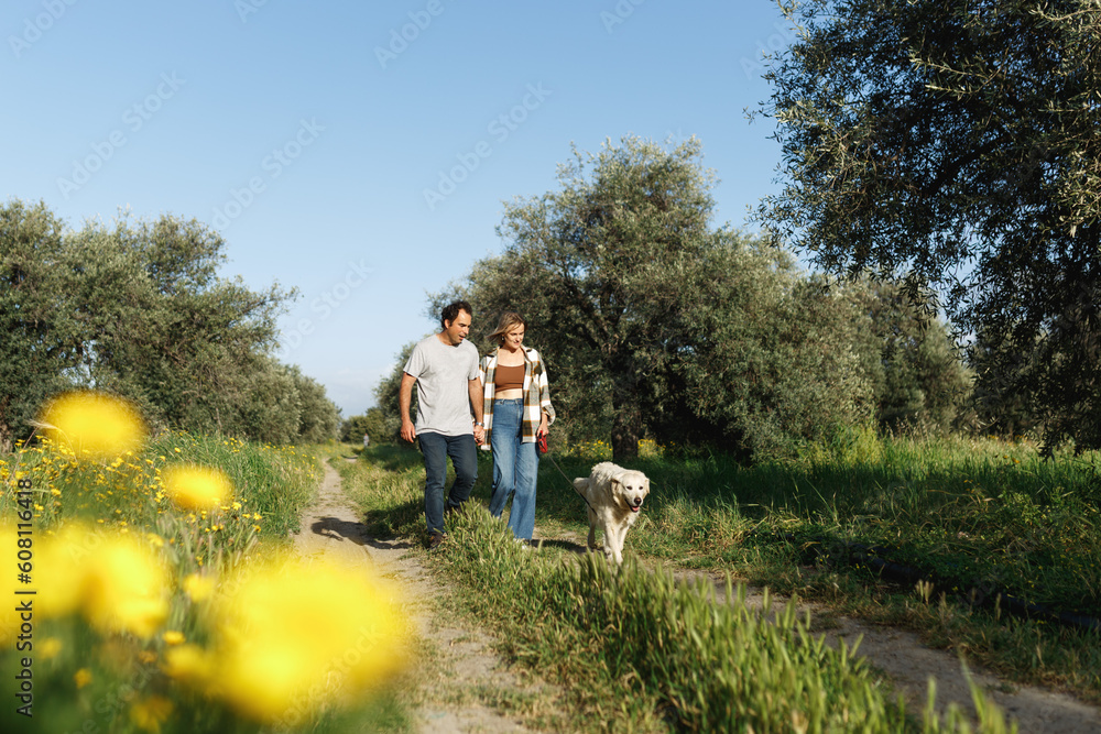 Couple with pet ,golden retriever dog, walking along path across field in countryside in Cyprus Couple with pet ,golden retriever dog, walking along path across field in countryside in Cyprus