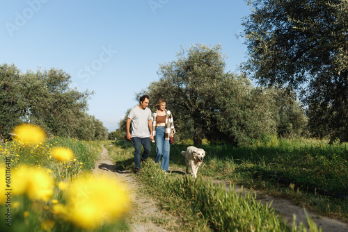 Couple with pet ,golden retriever dog, walking along path across field in countryside in Cyprus